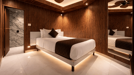 Wide angle view of the Executive Comfort room at Shakuntalam Hotels featuring a king bed with dark accent pillows wooden wall panels ceiling fan and warm ambient floor lighting.