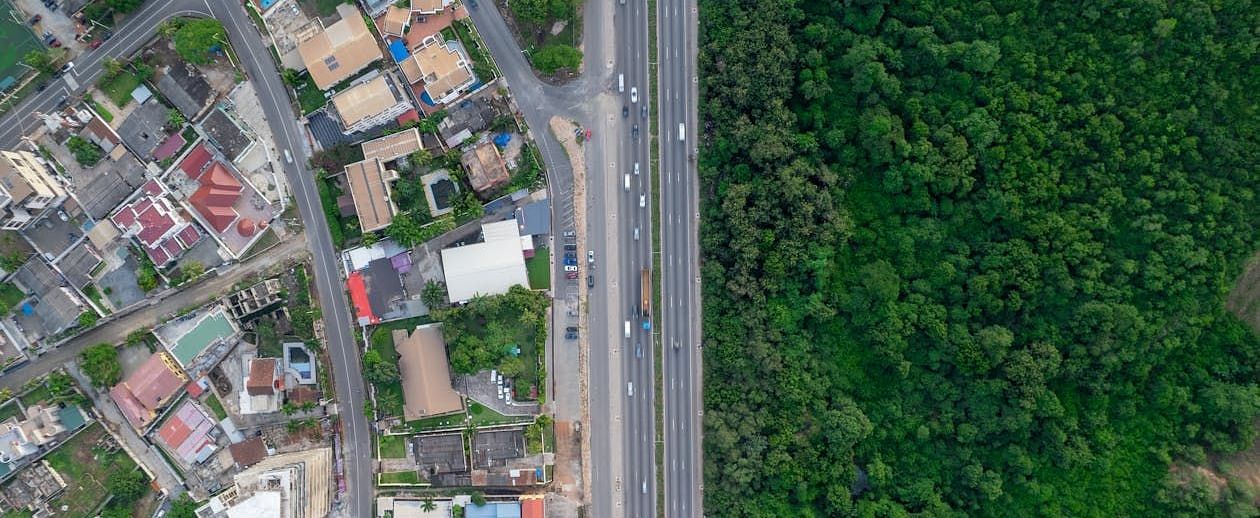 Aerial view showing the urban landscape meeting dense greenery, with a major road cutting through both city and forest.