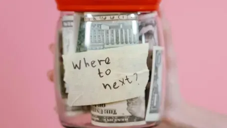 A glass jar filled with money and a handwritten note asking 'where to next?'.