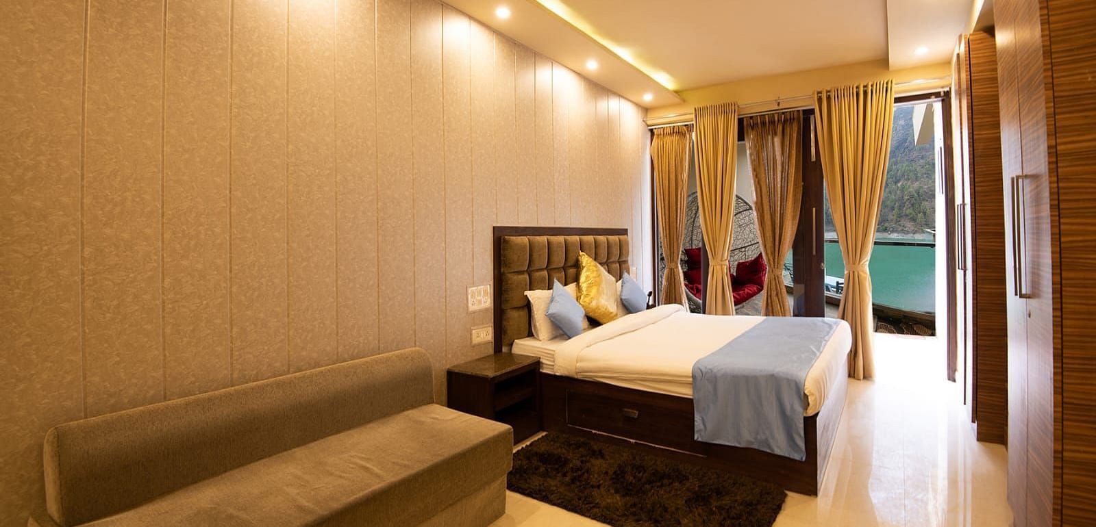 Spacious room featuring a bed, wall-mounted TV, sofa, and balcony view through glass doors.