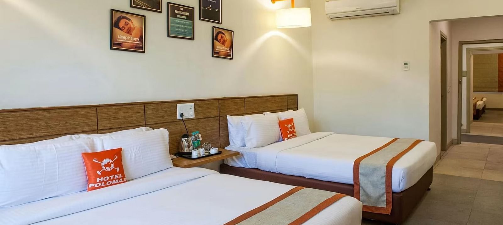 full view image of the max family room featuring two plush double beds along with a split air-conditioner and a bedside table between the two beds - Max Hotel Jabalpur