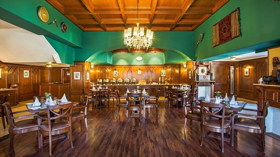 An image showing the interior of restaurant at The naini retreat, Nainital. featuring wooden decor, flooring, and a wooden bar. A large chandelier hangs from the ceiling, providing ambient lighting.