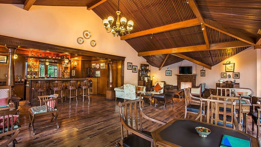 A bar and lounge area in naini retreat, nainital. The room features a wooden bar, comfortable seating arrangements, a fireplace, and a television. The overall ambiance is warm and inviting.