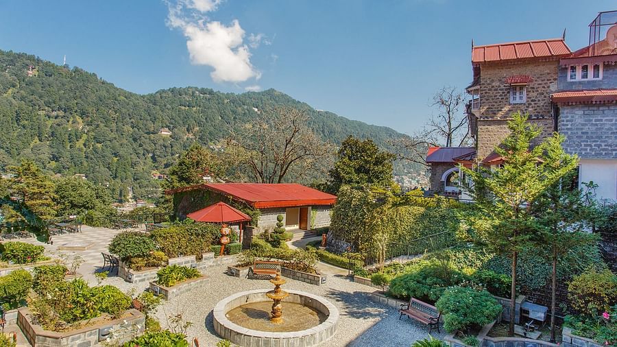 An image of the  garden with a fountain in the middle, with roofs of cottages visible, with a backdrop of the mountains.