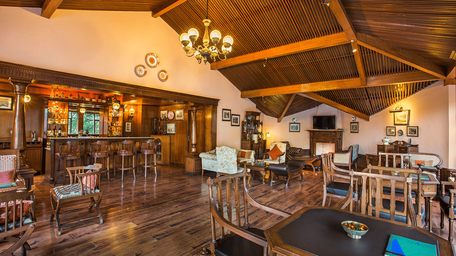 A bar and lounge area in naini retreat, nainital. The room features a wooden bar, comfortable seating arrangements, a fireplace, and a television. The overall ambiance is warm and inviting.
