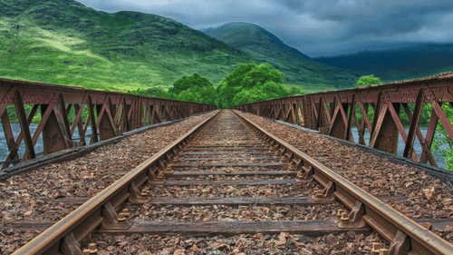 Railway track surrounded by mountains and abundant greenery.