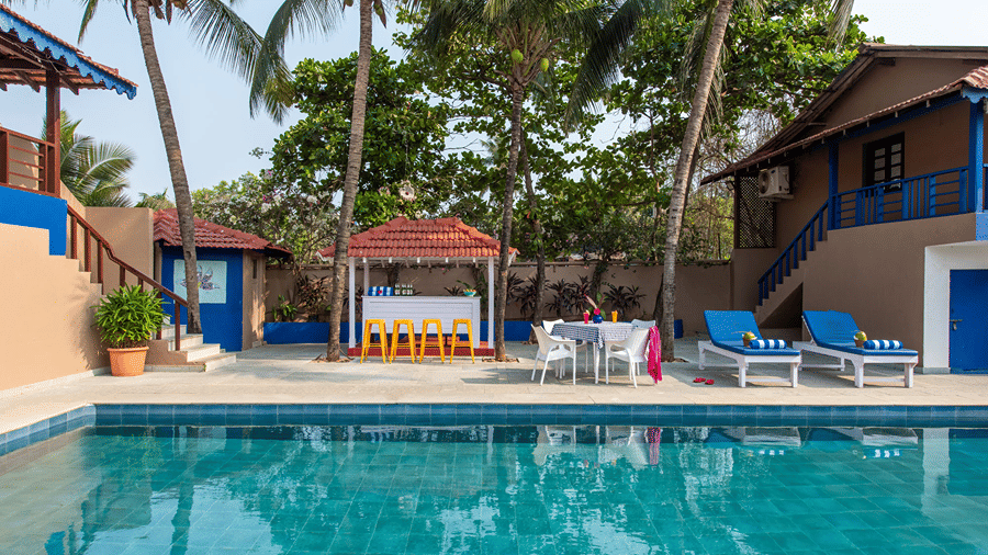 Outdoor swimming pool surrounded by palm trees, cottages and sun loungers.