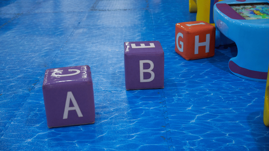 Soft toy blocks with alphabet letters are scattered on the floor of the Tic Tac Tot play area.