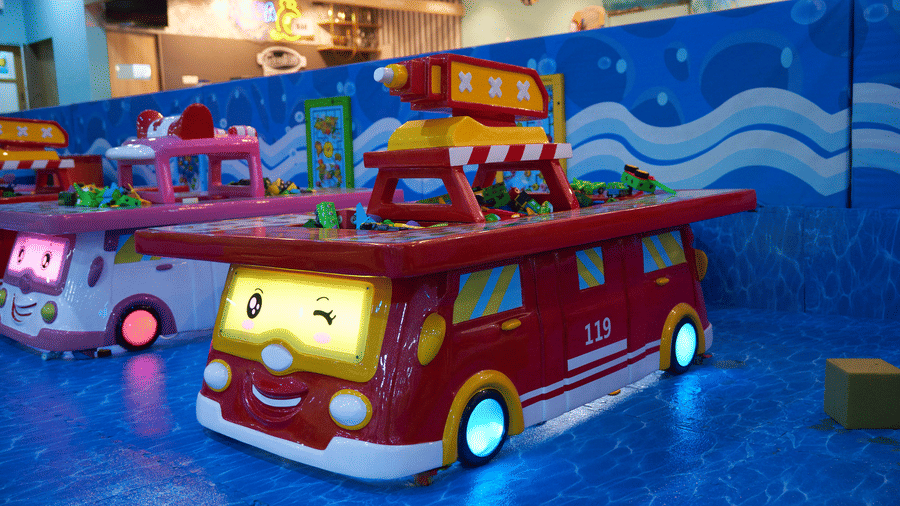 A toy fire truck play structure with wheels sits on the floor inside the Tic Tac Tot play area.