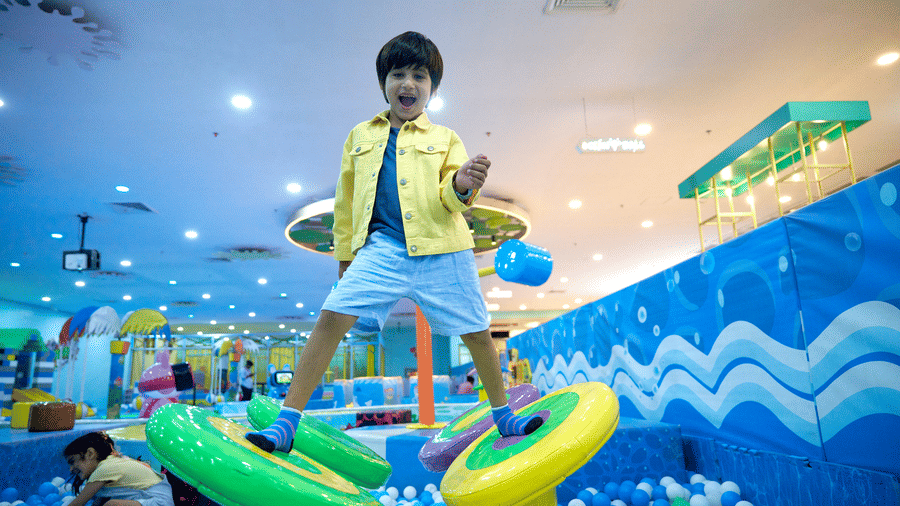 A young boy stands smiling on a round stepping platform over a ball pit at Tic Tac Tot.