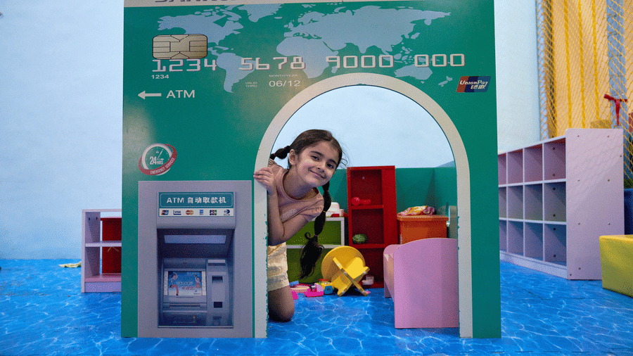 A young girl peeks out from a play bank card and ATM structure inside the Tic Tac Tot indoor playground.