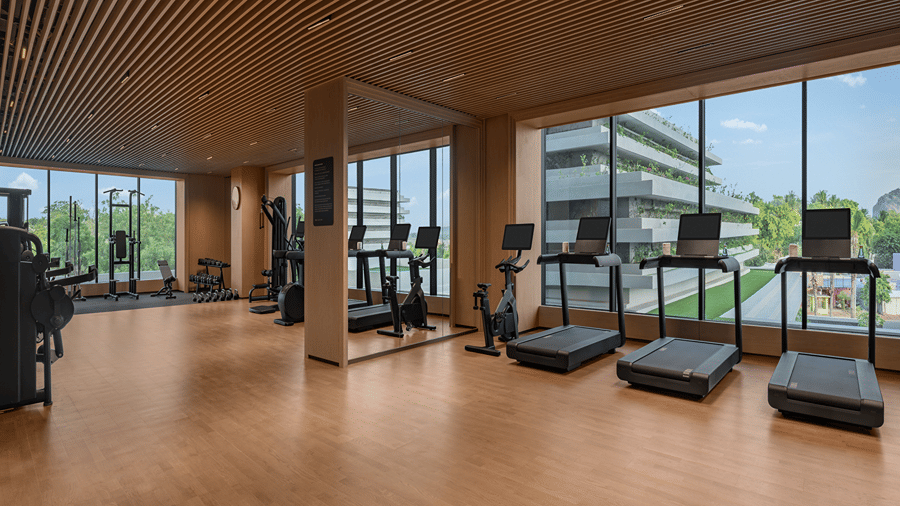 Gym with treadmills and cardio equipment set against large windows with a city view at The Residency Signature Madurai.