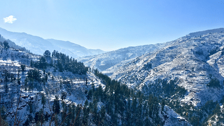 Panoramic view of Shimla, a Delhi-nearby hill station, on a sunny day featuring snow-clad slopes and valleys