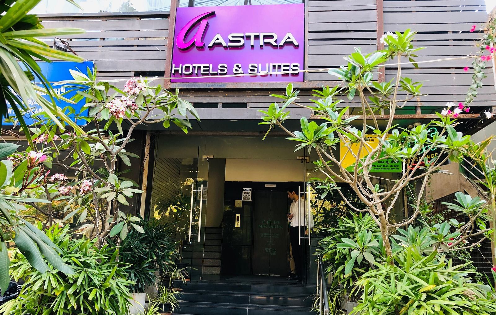 Entrance shot of Astra Hotels and Suites, HSR Sector 1 decorated with lot of plants and a sign board of the hotel.