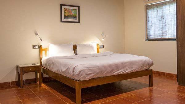 A bedroom with a wooden bed frame, white linens, and a small picture on the wall.