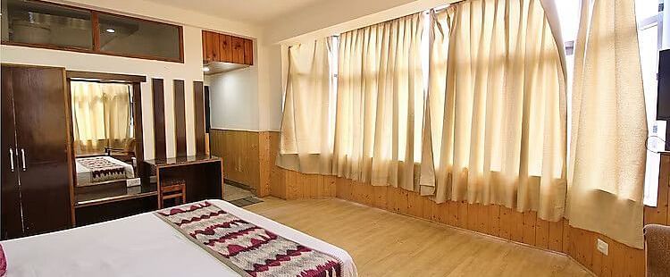A view of a room at DLS Hotel Devlok, Manali with a double bed and windows covering the wall in front of the bed