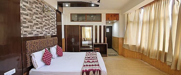 A view of a room at DLS Hotel Devlok, Manali with a double bed, side tables, a wardrobe with a mirror and  large windows