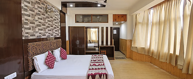 A view of a room at DLS Hotel Devlok, Manali with a double bed, side tables, a wardrobe with a mirror and  large windows