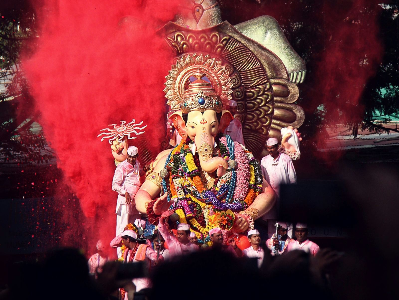 A decorated idol of Lord Ganesha surrounded by red powder with people standing in front.