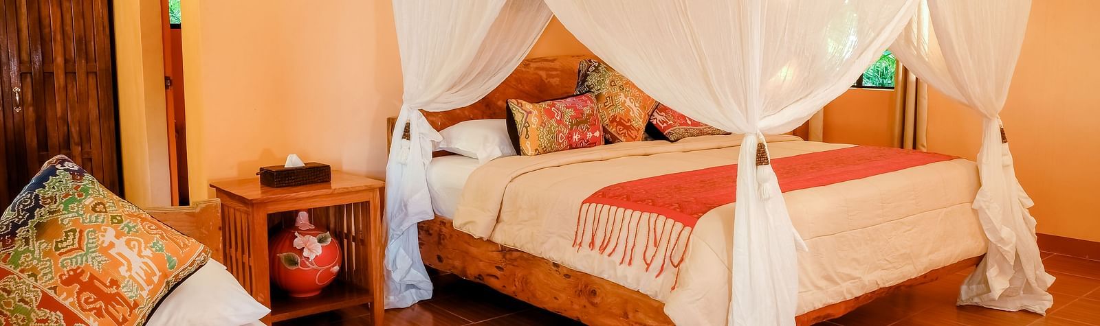 Room at Flower Island Resort with a canopy bed, pillows, wooden nightstand, and soft lighting.