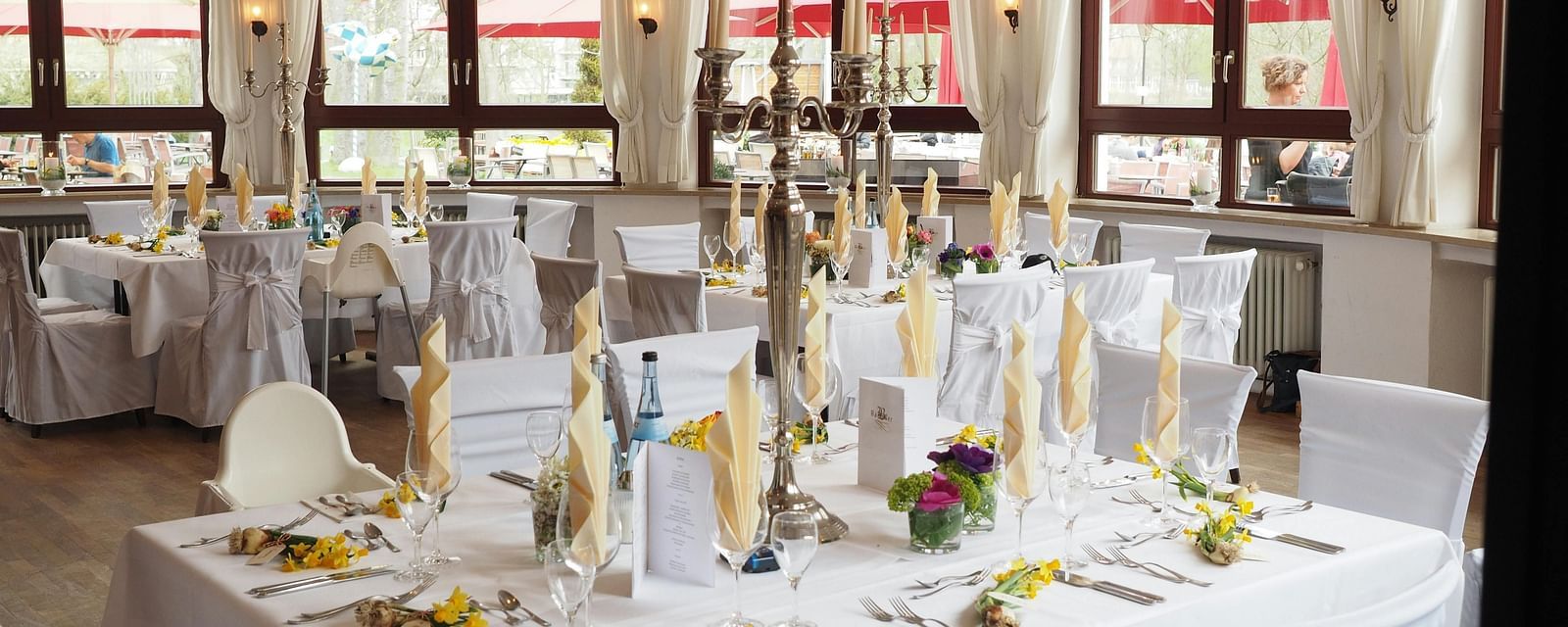 A image of a banquet hall that is illuminated in ambient yellow lighting and round tables covered in white linen cloth