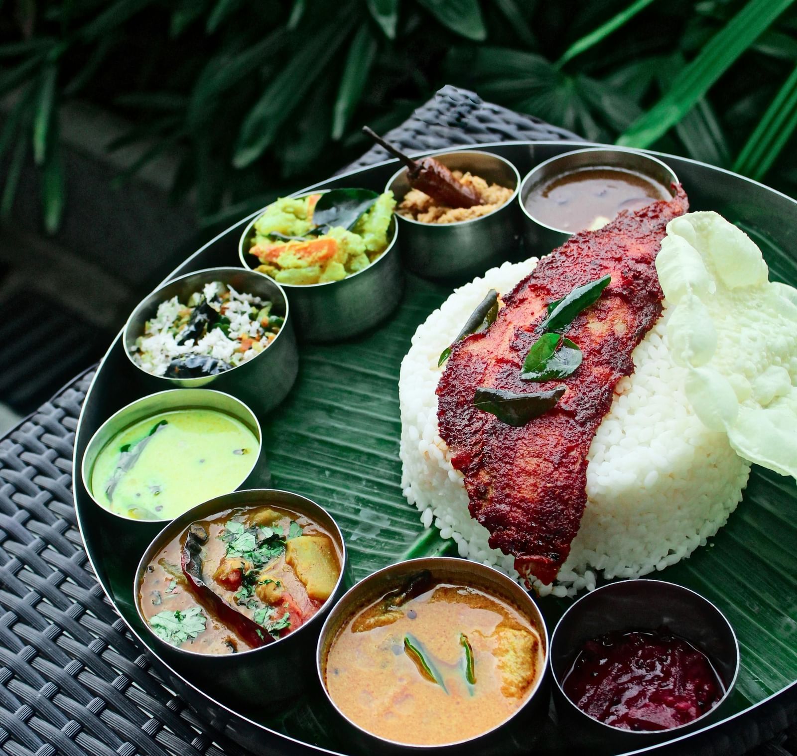 A plate lined with a banana leaf featuring a well-plated South Indian meal kept on a table.