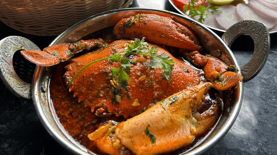 A crab curry dish in a metal bowl served alongside a basket of flatbreads and a salad plate at Oceanature Resort, Alibaug.