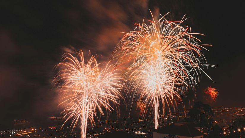 A view of firecrackers bursting in the sky with the city's landscape in view during the night.