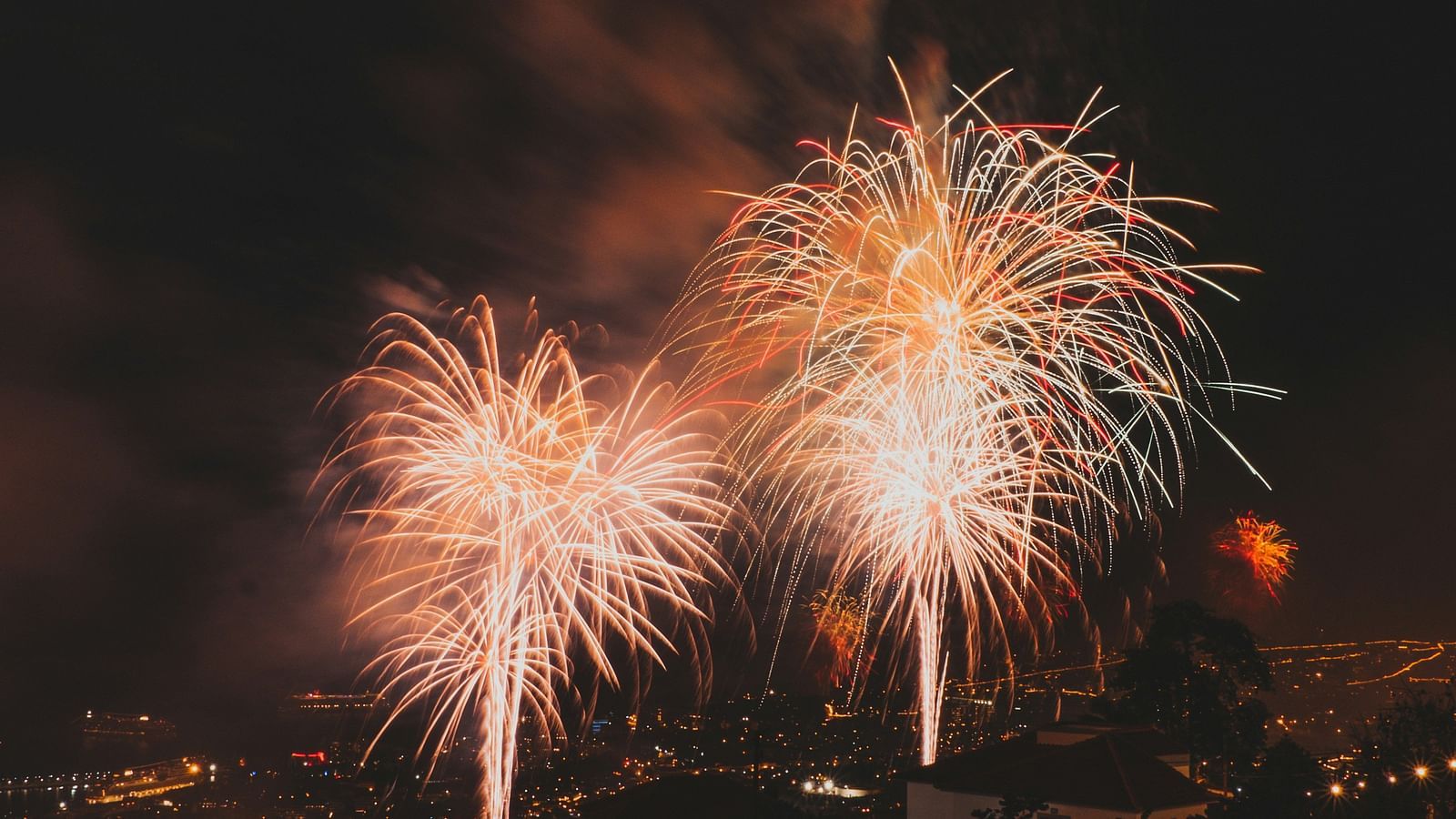 A far out view of a firecrackers being burst in the sky in night time illuminating the sky