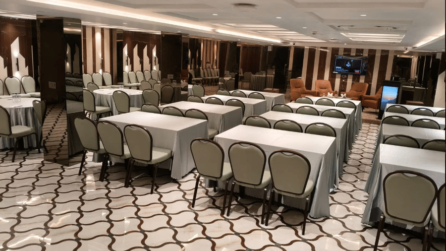 A meeting room with several rectangular tables covered in grey cloths and matching chairs on a patterned tile floor | Lawrence Solitaire Resort, Nainital
