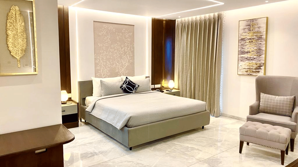 An image of a room with a well made king-sized bed, elegant decor, marble flooring, warm lighting, and a cosy chair - The Manohar, Hyderabad