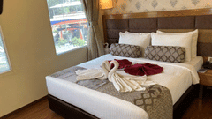 A hotel room with a large bed, decorative swan towels, and a view of the outside at Ramanashree Richmond.