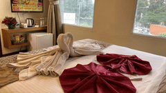 A bright hotel room with a TV and decorative towels on the bed.