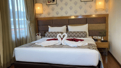 A hotel room with a neatly made bed and decorative towels shaped like swans at Ramanashree Richmond.