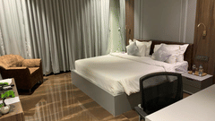 A hotel stay in Jamnagar featuring a plush bed with a work desk and a seating space next to the curtained window at VITS Jamnagar, Mithoi