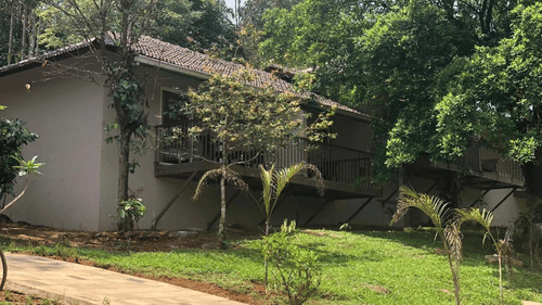 A building is nestled in a green landscape with a pathway leading to it, highlighting its natural surroundings. - Abad Brookside Lakkidi, Wayanad