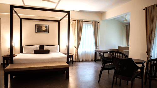 A spacious bedroom with a four-poster bed, elegant decor, and large windows at Abad Brookside Lakkidi, Wayanad.