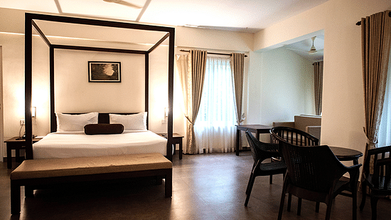 A spacious bedroom with a four-poster bed, elegant decor, and large windows. - Abad Brookside Lakkidi, Wayanad