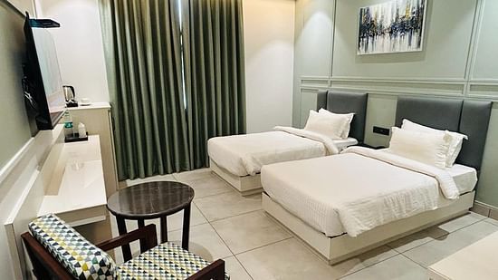 A room with twin beds, a sofa chair, coffee table, TV and a wall painting - Five Elements Hotels Goldleaf, Haldwani