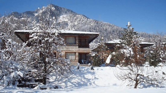 Snow-covered cottage at Lamrin Banon Resorts, Manali with scenic mountain backdrop.