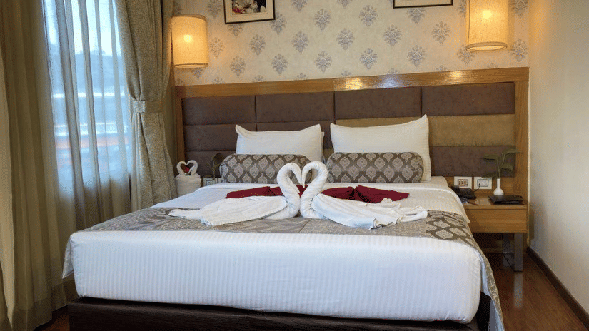 A hotel room with a neatly made bed and decorative towels shaped like swans.