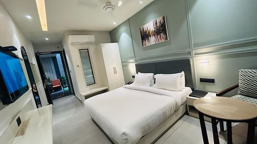 A room with a neatly made bed, a wall painting, a TV, a side drawer and a sofa chair - Five Elements Hotels Goldleaf, Haldwani
