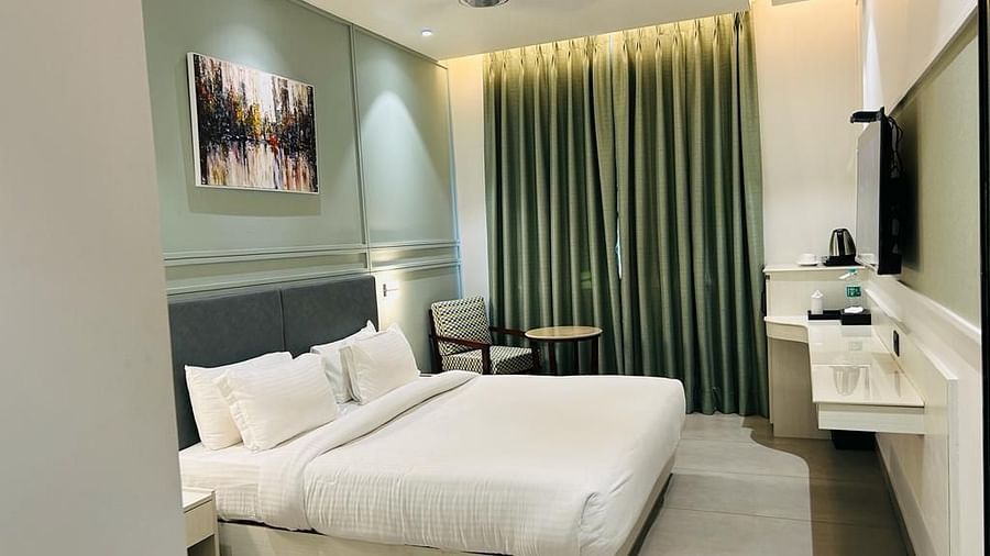 A room with a neatly made bed, a wall painting, a TV, a tea & coffee maker and a sofa chair - Five Elements Hotels Goldleaf, Haldwani