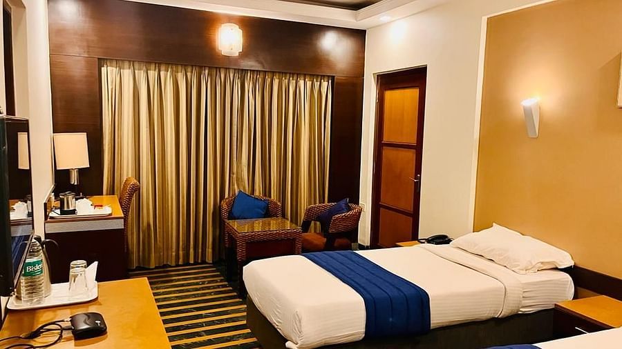 Twin-bed hotel room with warm lighting, wooden furniture, and a seating area near the window at Hotel Dr. Rajkumar International.
