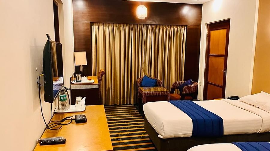 Side view of a twin-bed hotel room featuring a wall-mounted television, a wooden desk, and warm interior lighting at Hotel Dr. Rajkumar International.