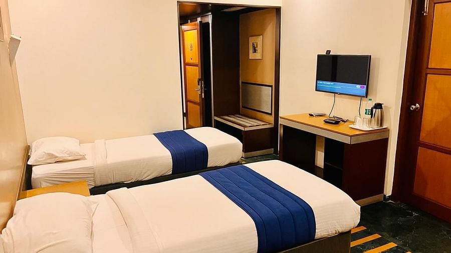 spacious twin-bed room with a wall-mounted TV, desk, and mirror, viewed from the entrance, at Hotel Dr. Rajkumar International.