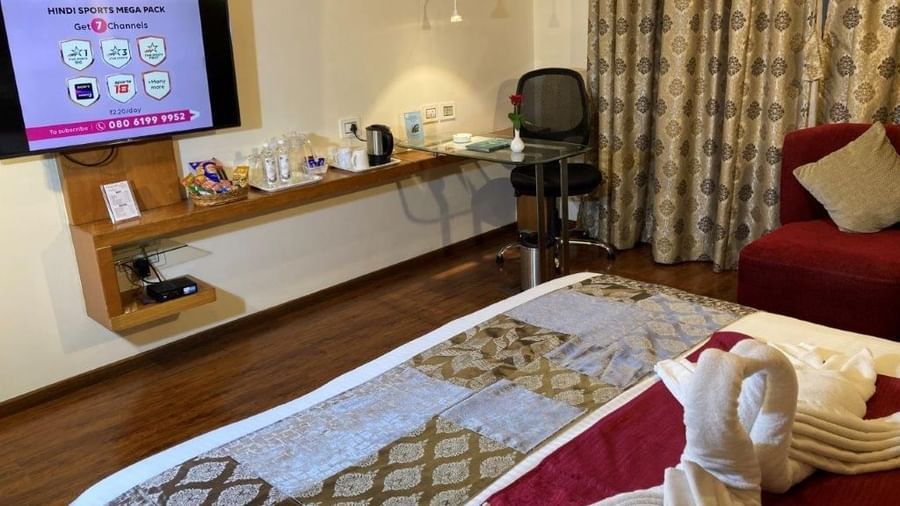 A hotel room with a wall-mounted TV and a coffee table with decorative towels on it.