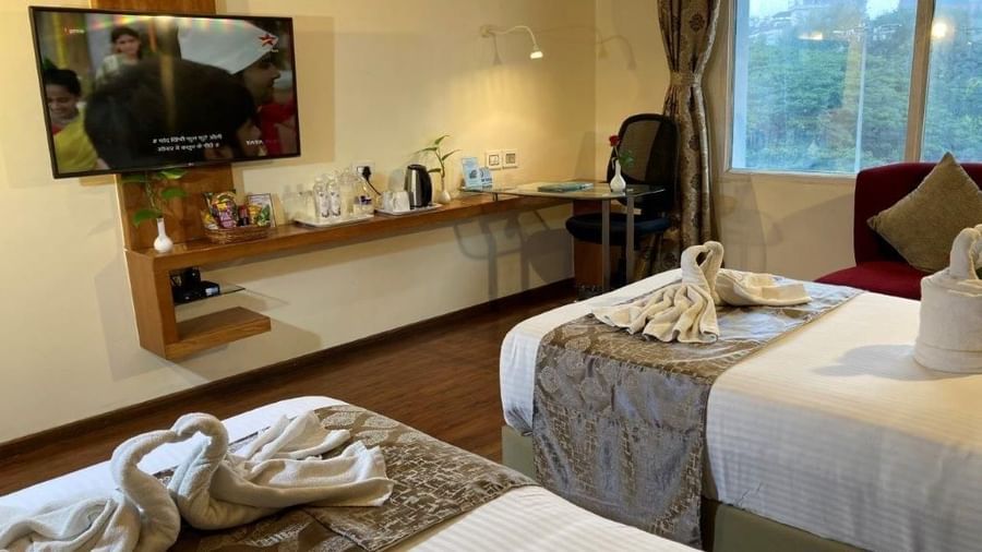 A hotel room with two beds and a wall-mounted TV.