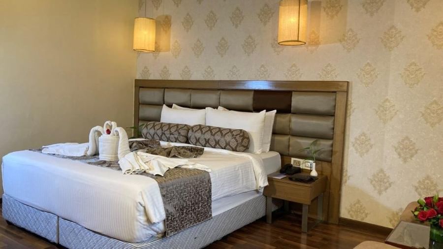 A hotel room with a neatly made bed and decorative towels on the bed and nightstands with lamps.