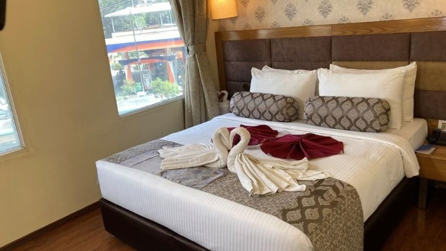 A hotel room with a large bed, decorative swan towels, and a view of the outside.